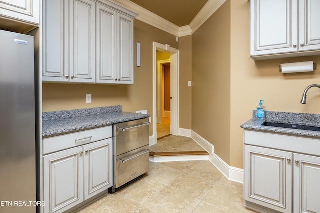 kitchen featuring sink, light stone countertops, ornamental molding, white cabinetry, and stainless steel refrigerator