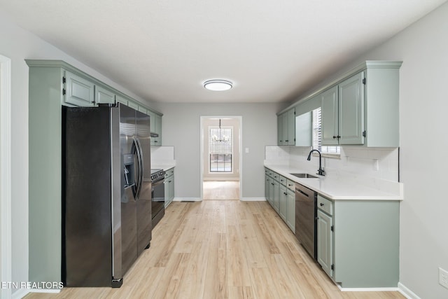 kitchen featuring decorative backsplash, appliances with stainless steel finishes, light wood-type flooring, sink, and a notable chandelier