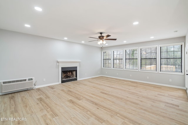 unfurnished living room featuring a wall unit AC, ceiling fan, plenty of natural light, and light hardwood / wood-style floors