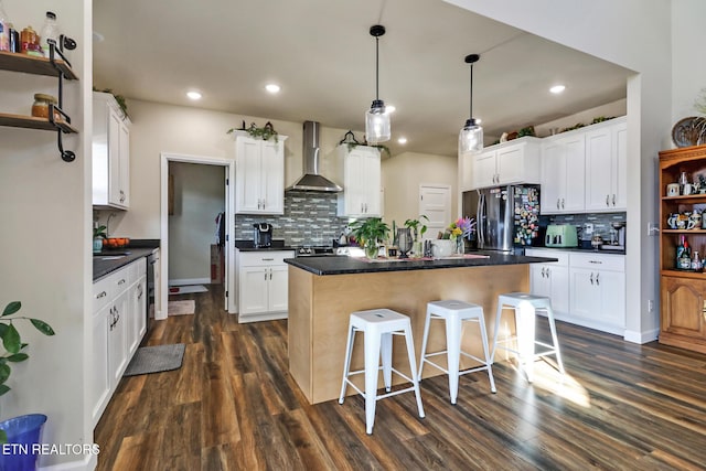 kitchen with stainless steel fridge, white cabinets, and wall chimney range hood