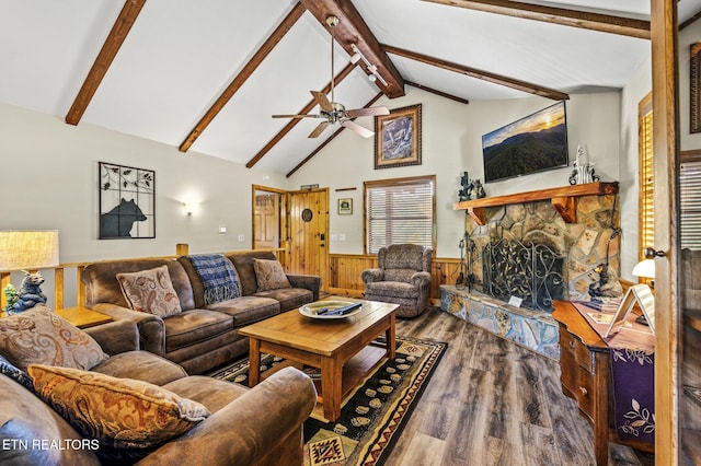 living room featuring ceiling fan, hardwood / wood-style floors, vaulted ceiling with beams, a stone fireplace, and wood walls