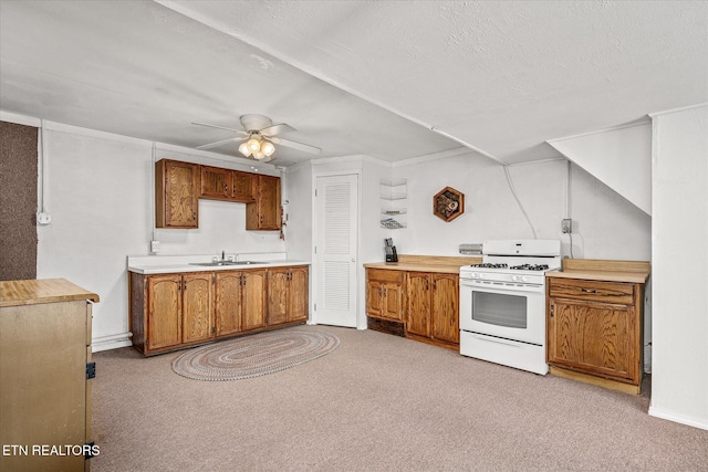 kitchen featuring a textured ceiling, light colored carpet, ceiling fan, white range with gas cooktop, and sink