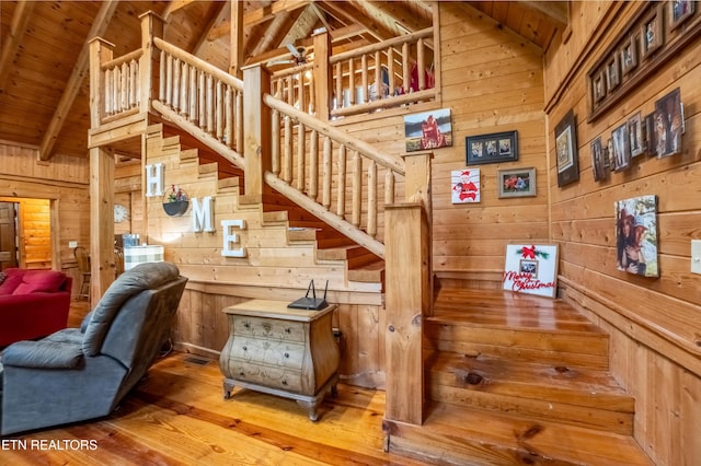 stairway featuring wooden walls, wood-type flooring, high vaulted ceiling, wooden ceiling, and beamed ceiling