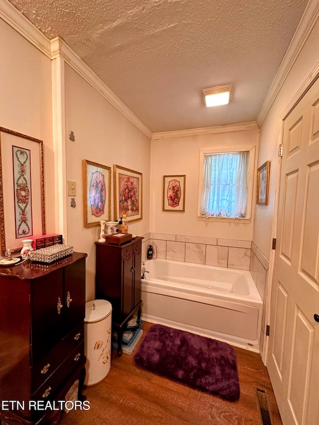 bathroom with a tub to relax in, hardwood / wood-style floors, a textured ceiling, vanity, and ornamental molding