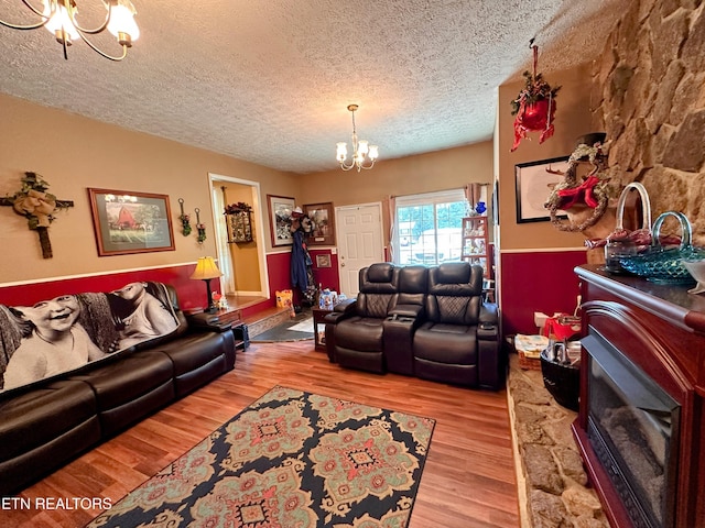 living room with a stone fireplace, light hardwood / wood-style floors, a textured ceiling, and a notable chandelier