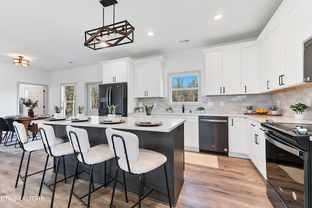 kitchen with black appliances, a kitchen island, white cabinetry, and hanging light fixtures