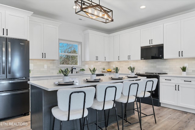 kitchen featuring pendant lighting, black appliances, light wood-type flooring, a kitchen island, and white cabinetry