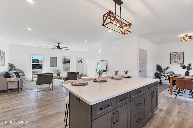 kitchen with a breakfast bar area, ceiling fan, decorative light fixtures, and light wood-type flooring