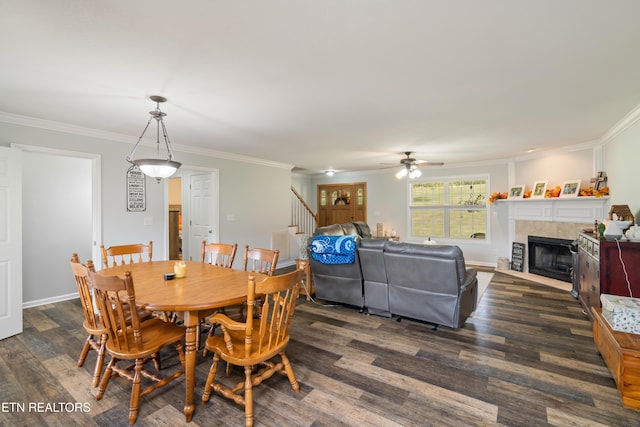 dining area featuring a tile fireplace, dark wood-type flooring, ceiling fan, and crown molding