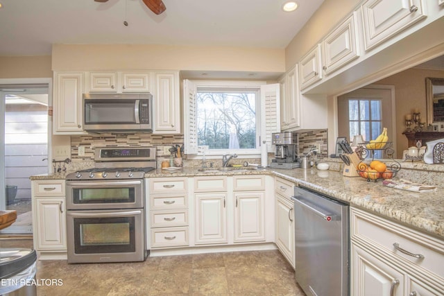 kitchen featuring appliances with stainless steel finishes, tasteful backsplash, light stone counters, and sink