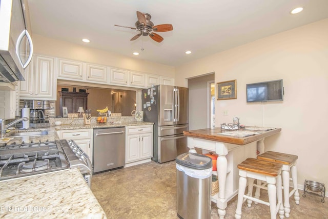 kitchen with light stone countertops, appliances with stainless steel finishes, a kitchen bar, ceiling fan, and sink