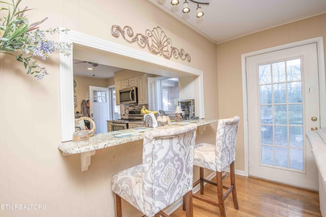 kitchen with backsplash, crown molding, light hardwood / wood-style flooring, kitchen peninsula, and a breakfast bar area