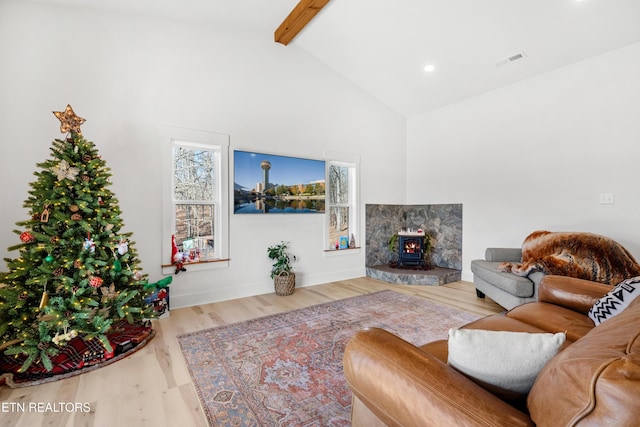 living room with beam ceiling, light wood-type flooring, a wood stove, and plenty of natural light