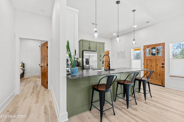 kitchen featuring a breakfast bar, sink, stainless steel fridge with ice dispenser, hanging light fixtures, and green cabinets