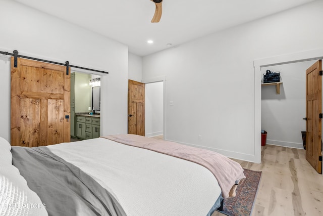 bedroom with a walk in closet, ensuite bath, ceiling fan, a barn door, and light hardwood / wood-style floors