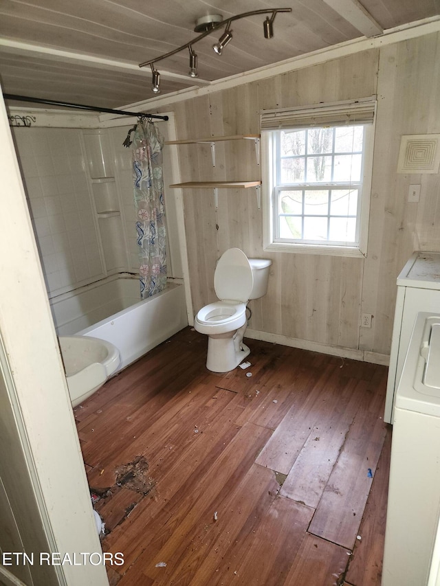 bathroom featuring washer / clothes dryer, hardwood / wood-style floors, toilet, wooden walls, and shower / bath combo with shower curtain