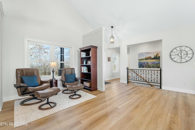 living area with a healthy amount of sunlight, high vaulted ceiling, and light hardwood / wood-style flooring