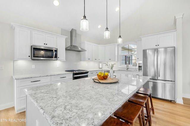 kitchen featuring white cabinets, a kitchen island, wall chimney exhaust hood, and appliances with stainless steel finishes