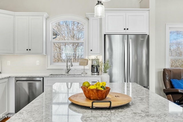 kitchen featuring white cabinetry, sink, light stone countertops, decorative light fixtures, and appliances with stainless steel finishes