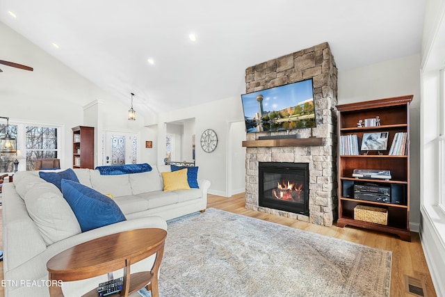 living room featuring ceiling fan, light hardwood / wood-style floors, a stone fireplace, and high vaulted ceiling