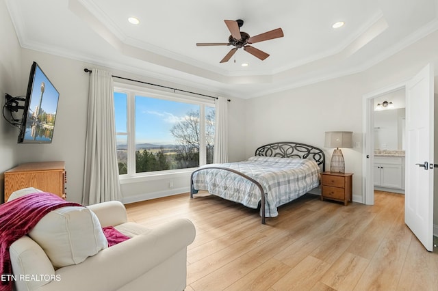 bedroom featuring a raised ceiling, ensuite bath, ceiling fan, ornamental molding, and light hardwood / wood-style floors