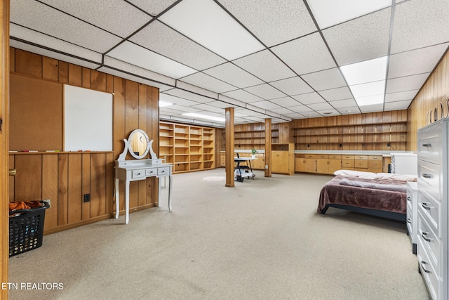 bedroom featuring a drop ceiling, wood walls, and light colored carpet