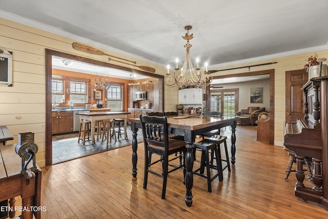 dining space with a chandelier, wood-type flooring, crown molding, and wooden walls