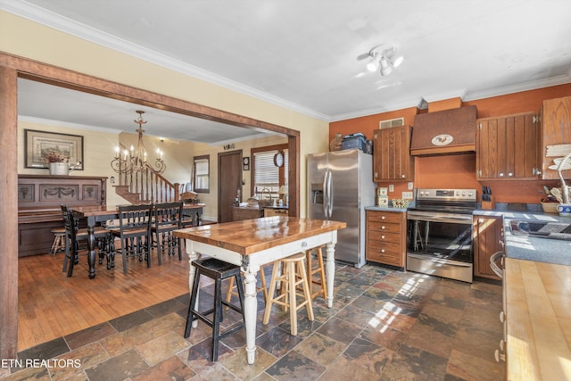 kitchen with stainless steel appliances, brown cabinetry, custom range hood, and an inviting chandelier