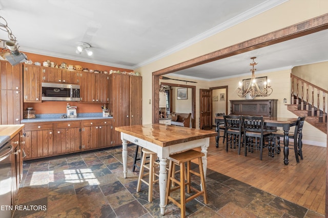 kitchen with crown molding, stone tile floors, stainless steel microwave, and brown cabinets