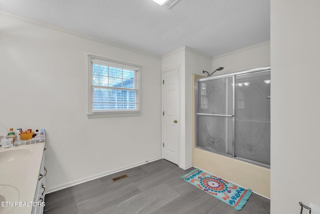 bathroom with a textured ceiling, vanity, ornamental molding, and bath / shower combo with glass door