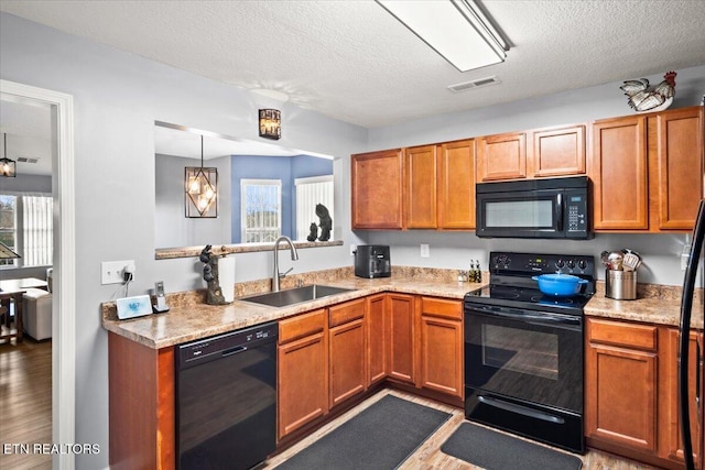 kitchen featuring black appliances, sink, a textured ceiling, decorative light fixtures, and light hardwood / wood-style floors