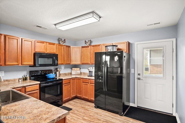 kitchen with black appliances, light hardwood / wood-style floors, sink, and a textured ceiling