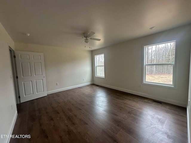 empty room featuring dark hardwood / wood-style flooring, a wealth of natural light, and ceiling fan