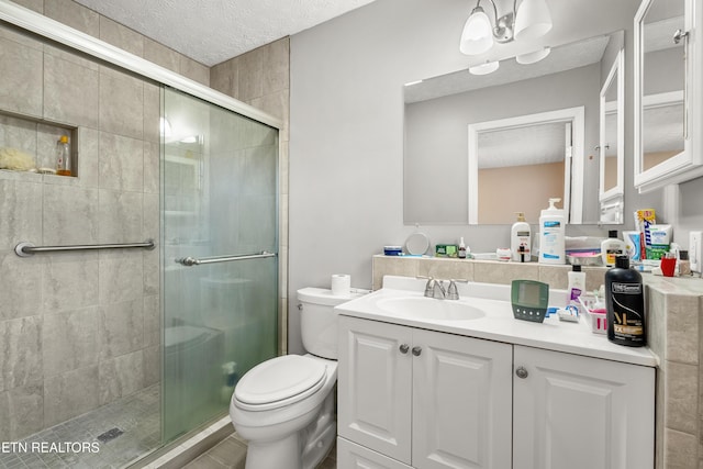 bathroom with vanity, toilet, a shower with shower door, and a textured ceiling