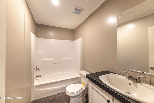 full bathroom with a textured ceiling, vanity, hardwood / wood-style flooring, washtub / shower combination, and toilet