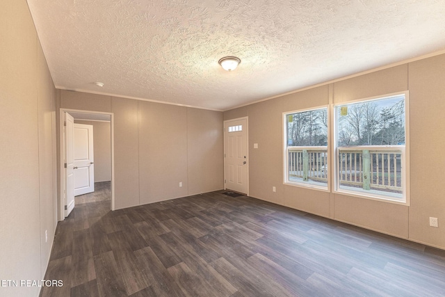 empty room featuring a textured ceiling, ornamental molding, and dark wood-type flooring