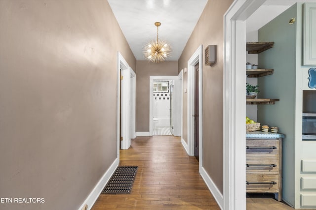 hallway featuring wood-type flooring and an inviting chandelier