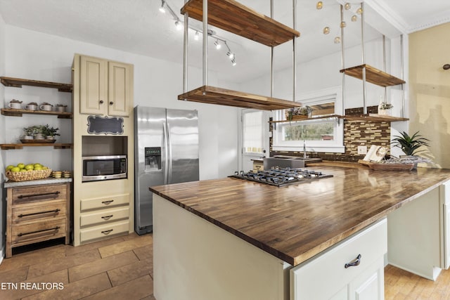 kitchen with cream cabinets, backsplash, stainless steel appliances, and butcher block counters