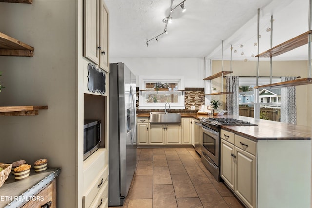 kitchen with sink, stainless steel appliances, backsplash, cream cabinets, and light tile patterned floors