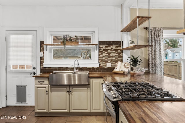 kitchen with sink, wood counters, tasteful backsplash, stainless steel range with gas cooktop, and light tile patterned floors