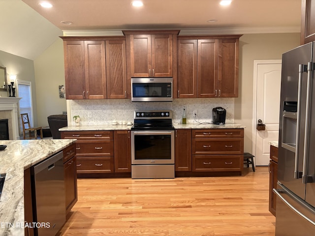 kitchen with tasteful backsplash, light stone counters, vaulted ceiling, stainless steel appliances, and light hardwood / wood-style floors