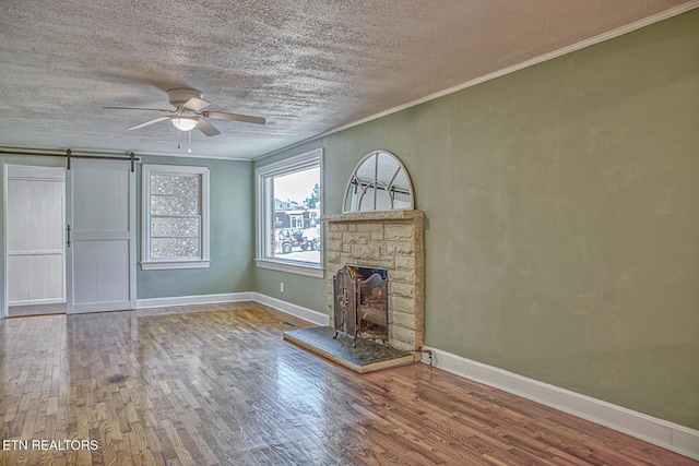 unfurnished living room featuring ceiling fan, crown molding, a textured ceiling, a fireplace, and hardwood / wood-style flooring