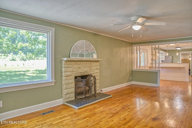 unfurnished living room with a textured ceiling, ceiling fan, crown molding, wood-type flooring, and a stone fireplace