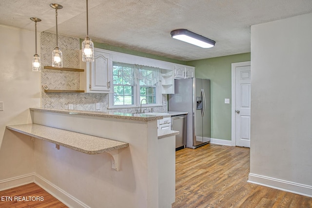 kitchen with kitchen peninsula, backsplash, a breakfast bar, stainless steel appliances, and white cabinetry