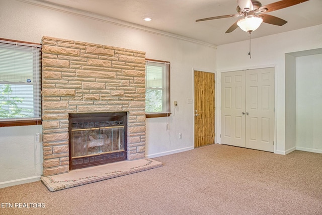 unfurnished living room featuring ceiling fan, a stone fireplace, carpet floors, and ornamental molding