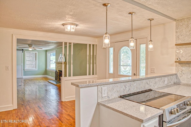 kitchen featuring kitchen peninsula, light stone counters, stainless steel electric stove, ceiling fan, and pendant lighting