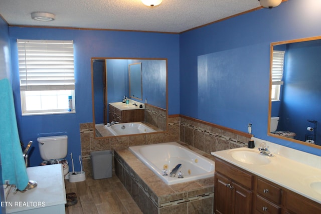 bathroom with a textured ceiling, vanity, hardwood / wood-style flooring, tiled bath, and toilet