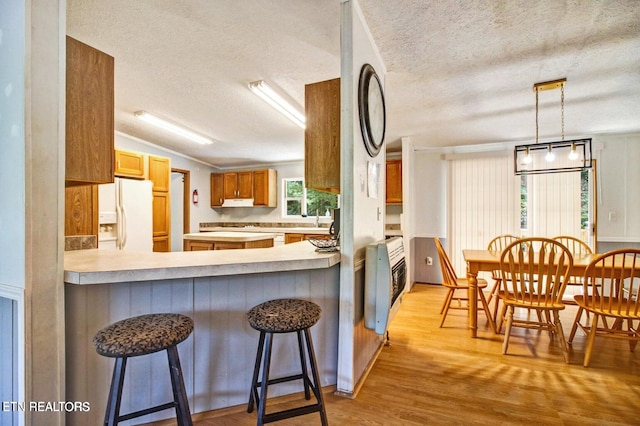 kitchen with white fridge with ice dispenser, a textured ceiling, light hardwood / wood-style floors, a kitchen bar, and kitchen peninsula