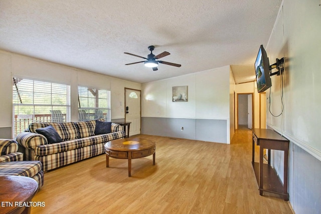 living room with ceiling fan, light wood-type flooring, and a textured ceiling