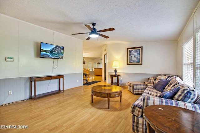 living room with a textured ceiling, light wood-type flooring, and ceiling fan